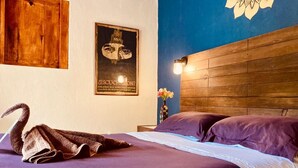 A bedroom with a wooden headboard, a bed with purple bedding, a decorative swan, a poster, and a vase with flowers.