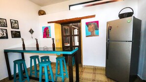 A kitchen with a stainless steel refrigerator, a blue bar stool set, and wall art.