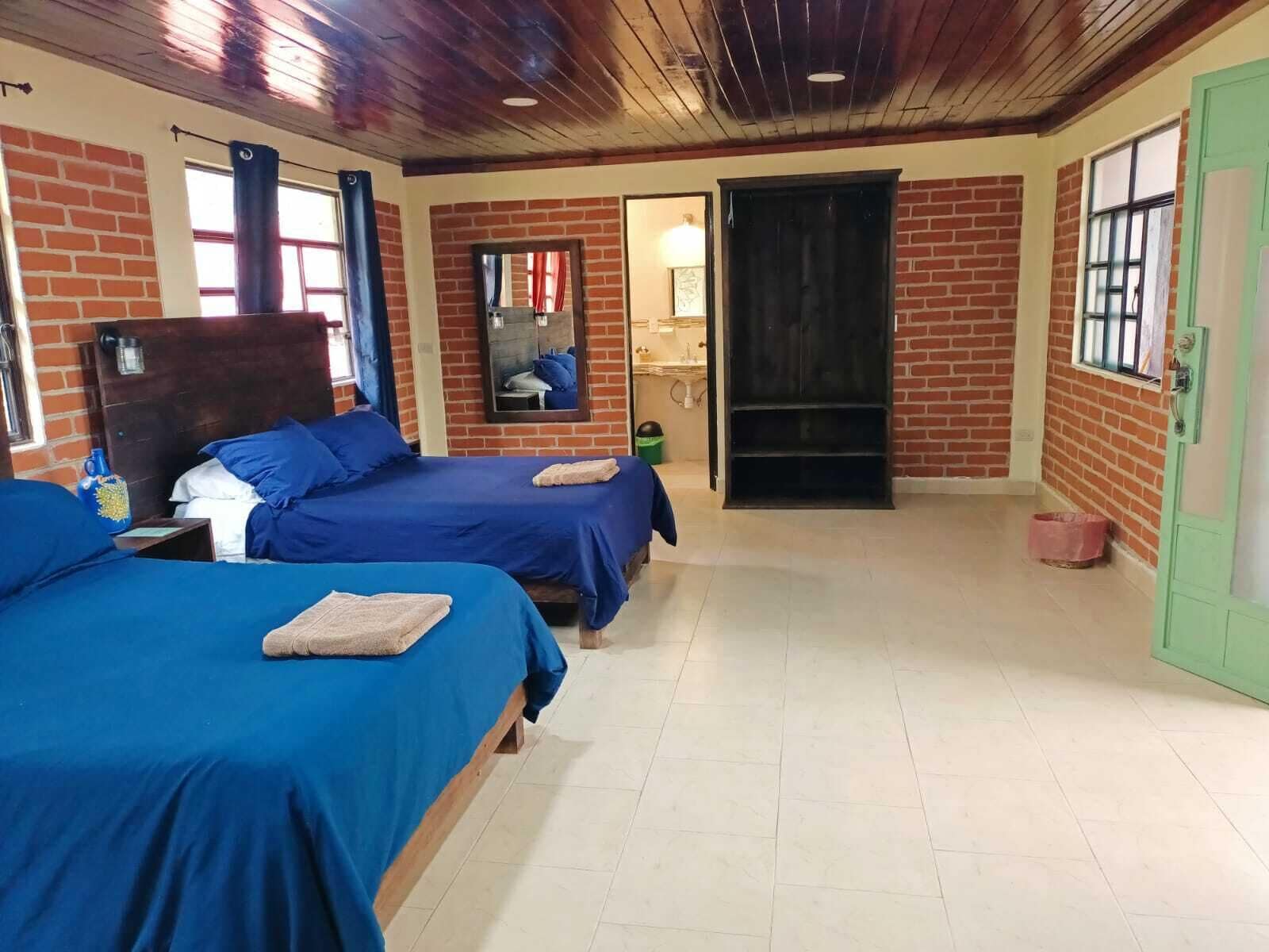 A room with two beds, a brick wall, a wooden ceiling, and a green door.