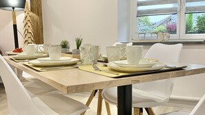 A dining area with a wooden table set for four, white chairs, and a window with blinds.