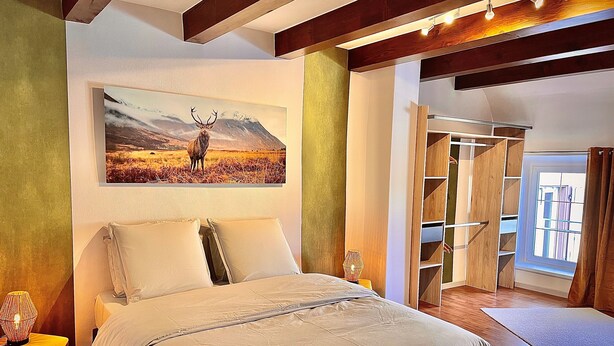 A bedroom with a bed, a painting of a deer, wooden shelving, and a window.