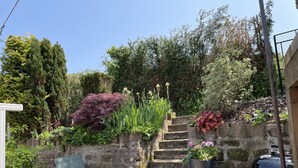 A stone staircase leading up to a garden area with various plants and a barbecue grill.