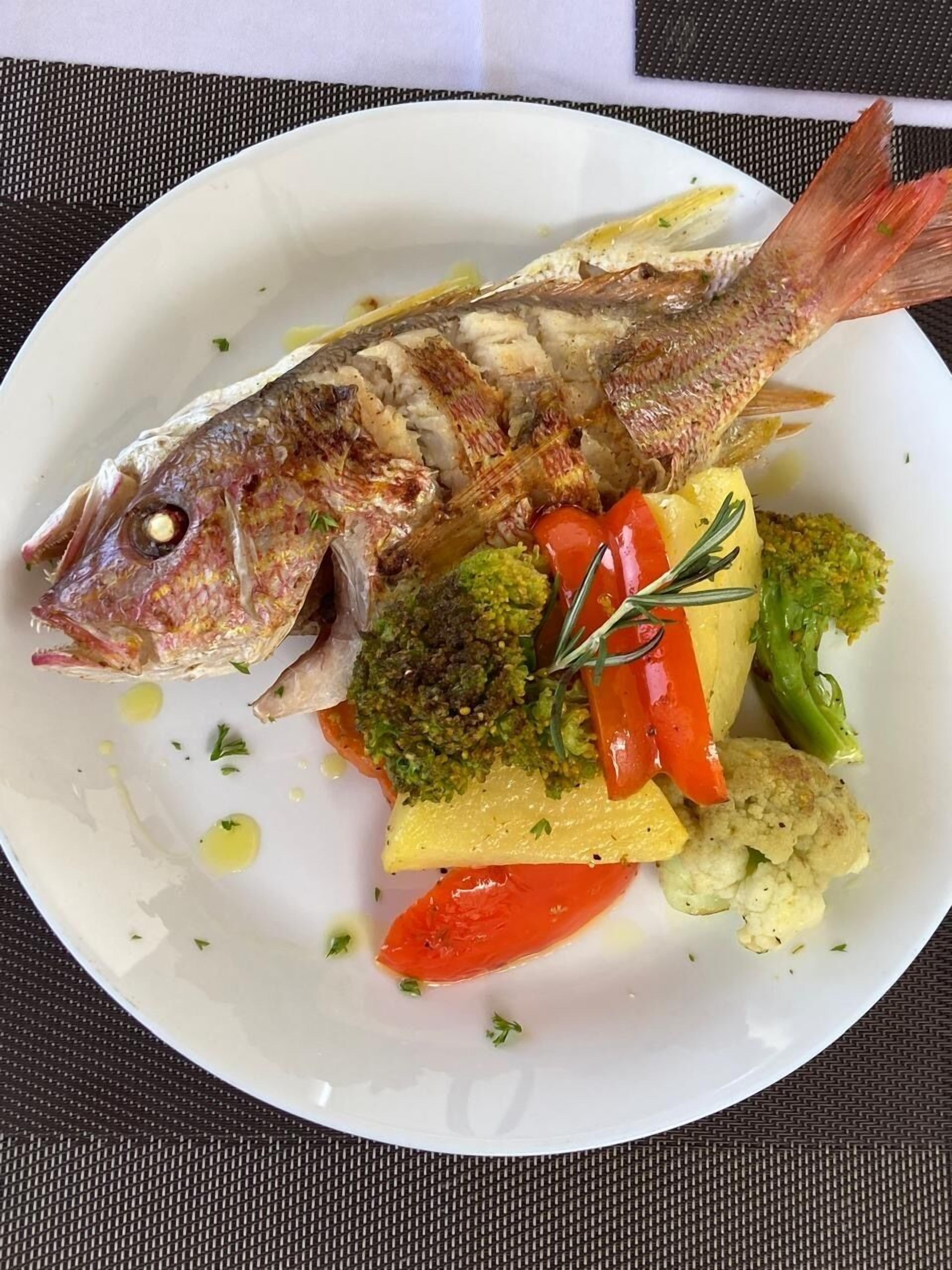 Een bord met gegrilde vis, broccoli, rode paprika en bloemkool.