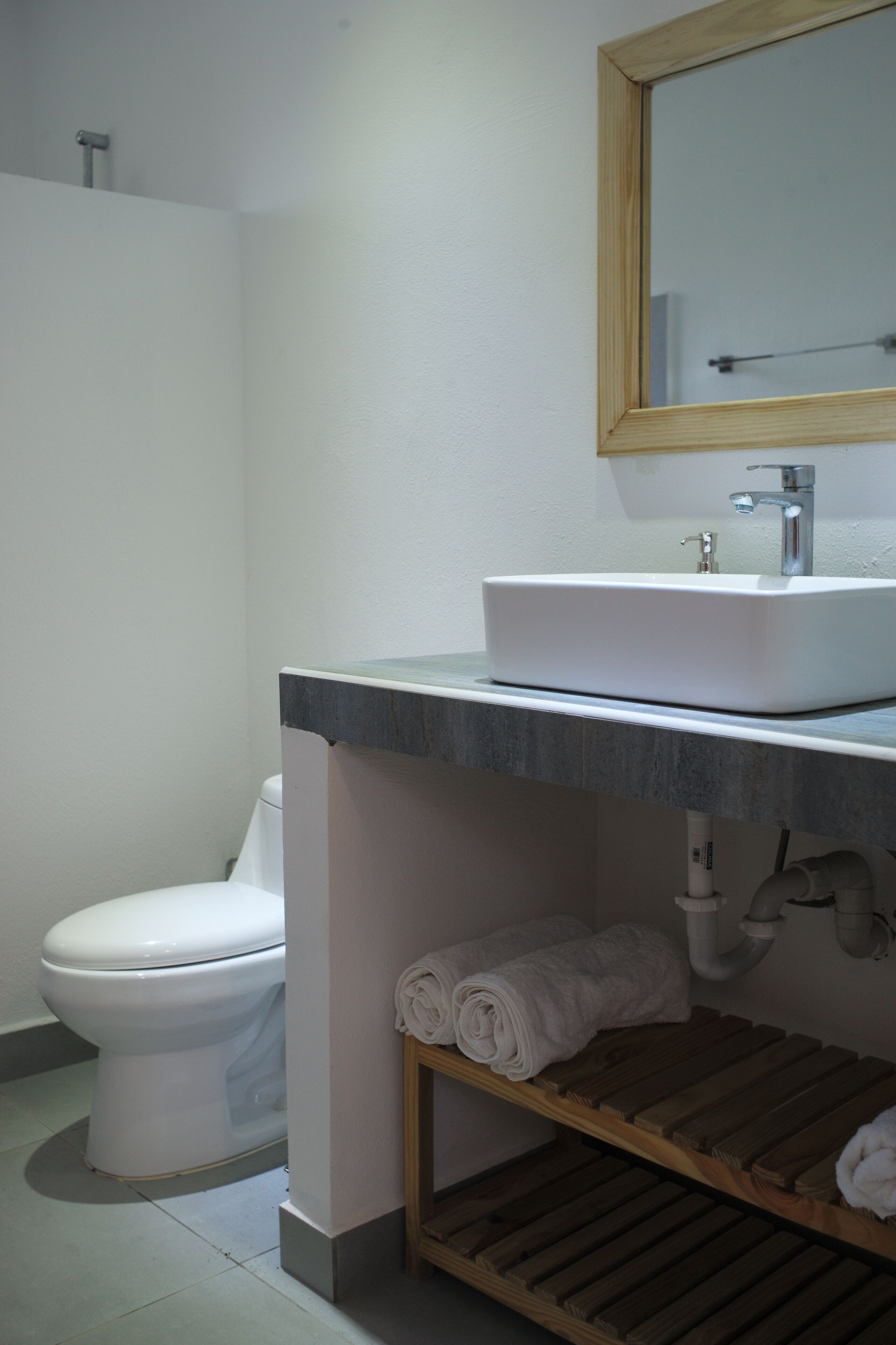 Un baño con lavamanos blanco, un espejo, un inodoro y un perchero para toallas.