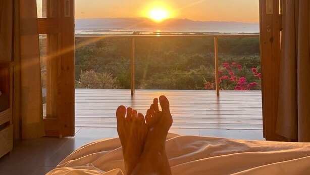 A bedroom with a large window, wooden floor, and a bed with white bedding. - Altos de la Caobita  (Azua)