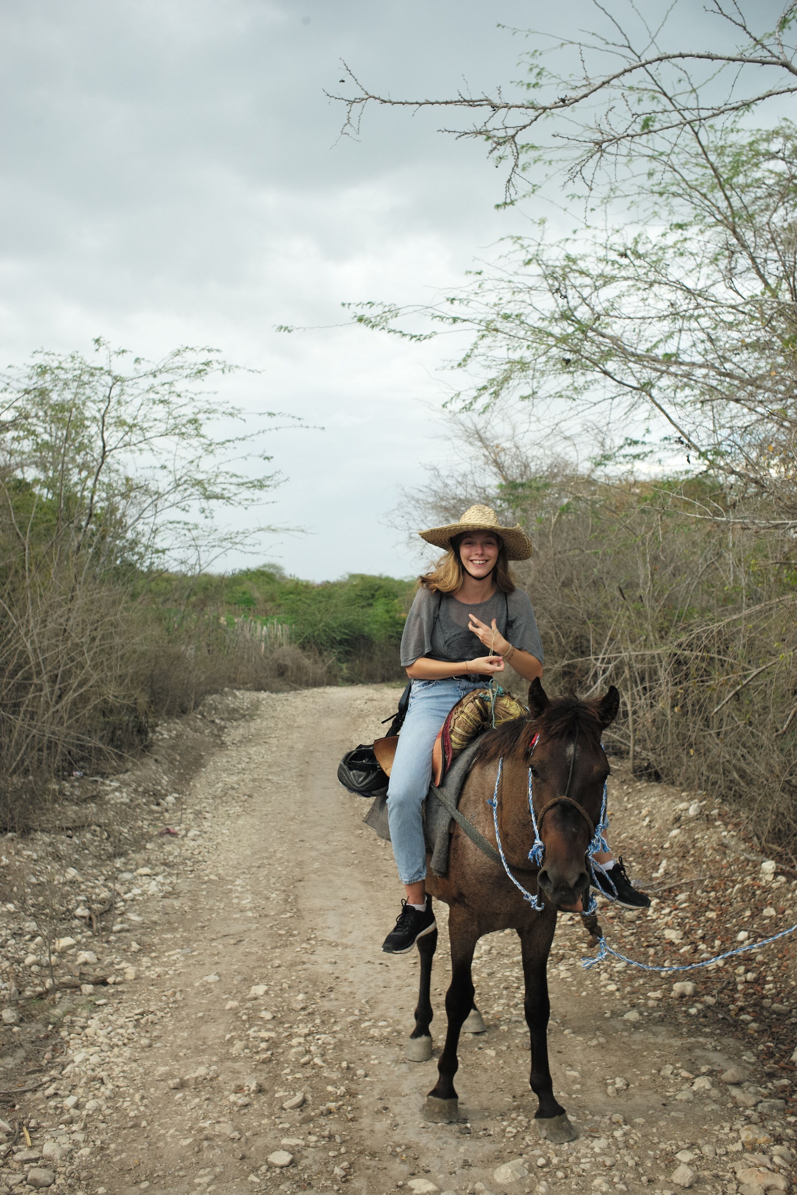 A person riding a horse on a dirt path surrounded by sparse vegetation.