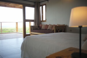 A bedroom with a bed, a nightstand, a lamp, a window, and a view of the outdoors.
