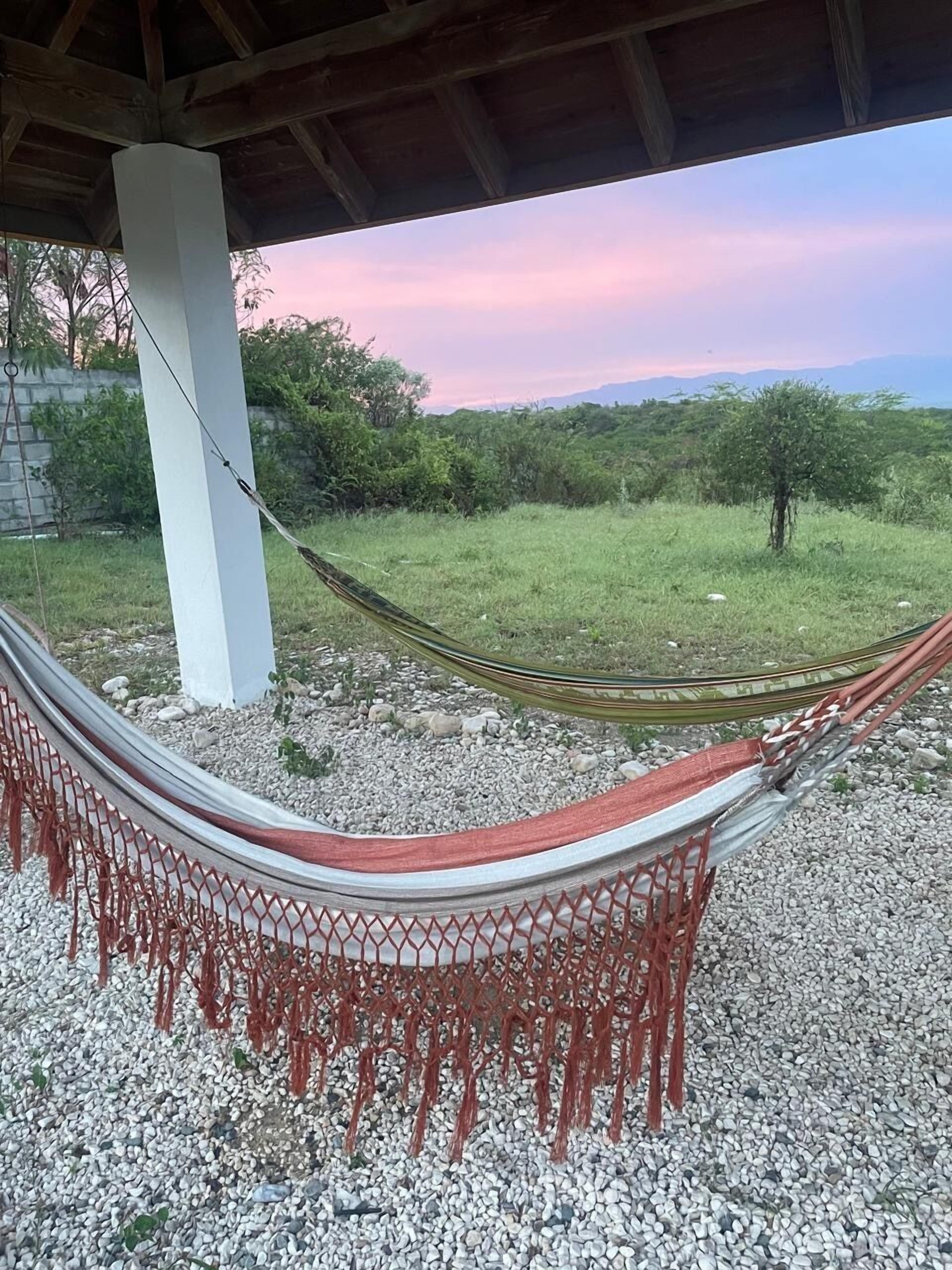 Una hamaca bajo una estructura de madera con vistas a un campo cubierto de césped y árboles.