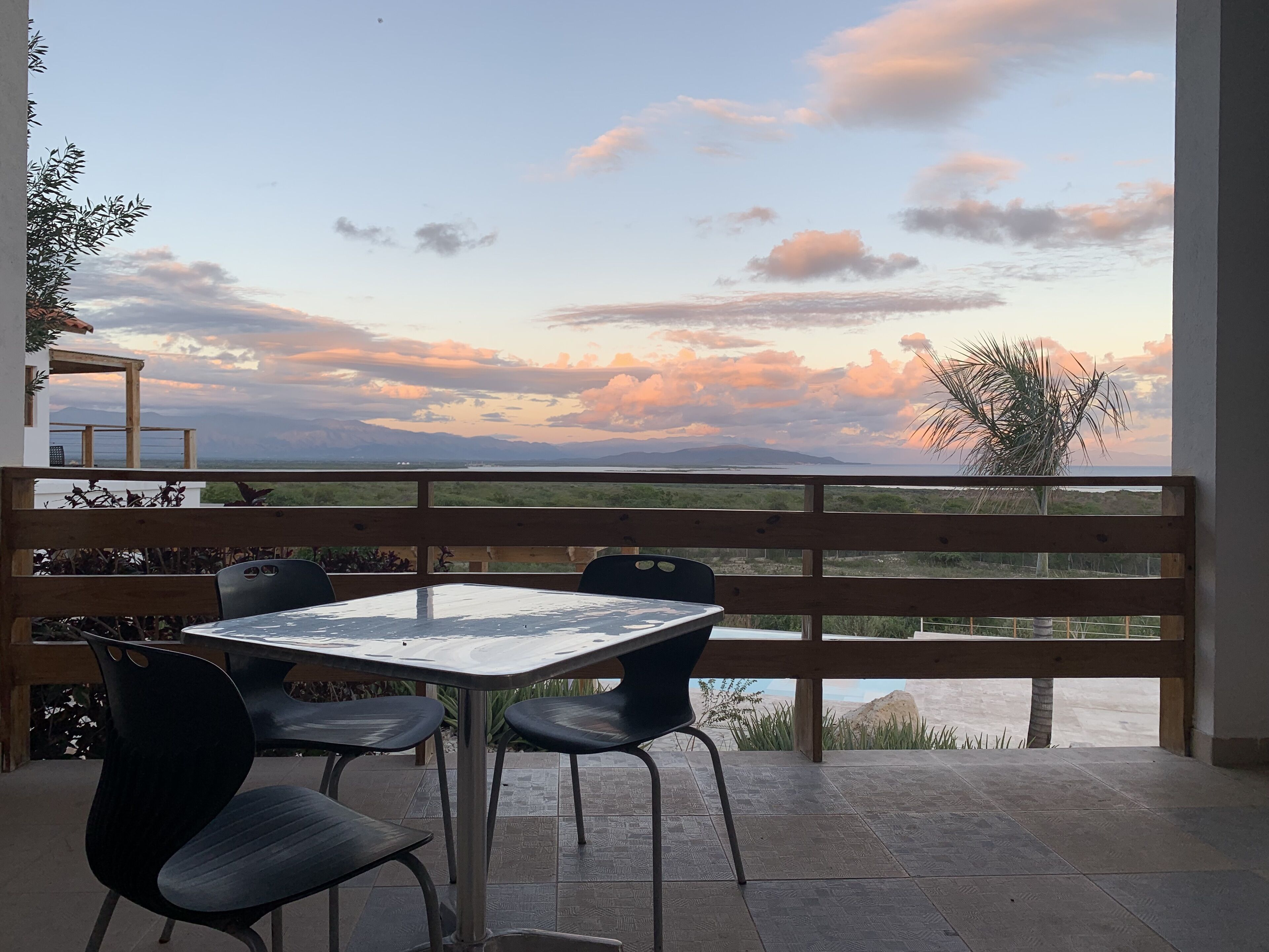 A terrace with a table and chairs, overlooking a scenic landscape with mountains and a sunset.