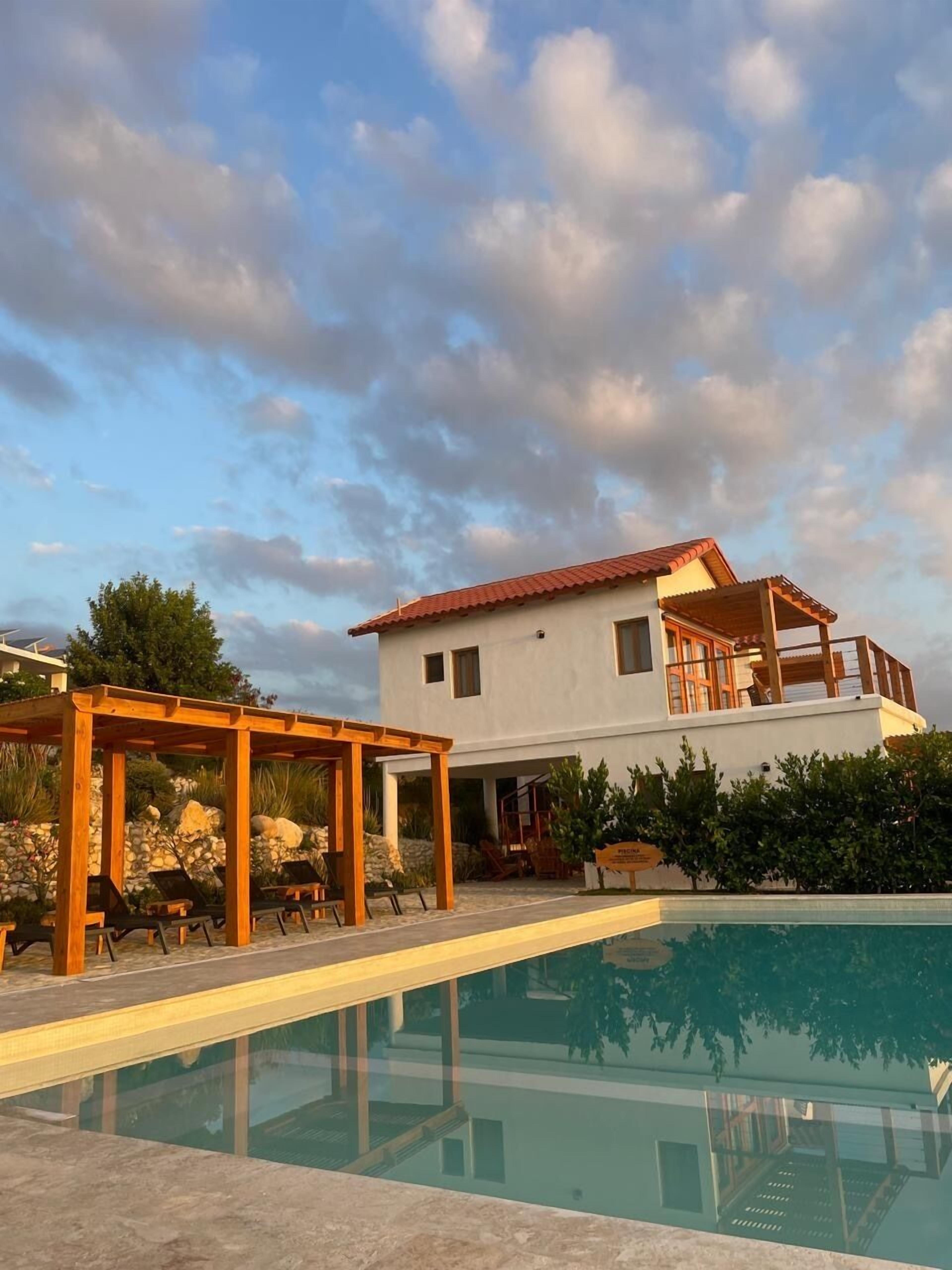 A modern two-story house with a swimming pool, wooden pergola, and outdoor seating.