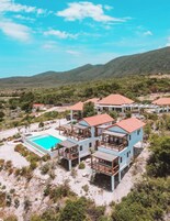 A resort with multiple buildings, a swimming pool, and a mountainous backdrop.