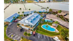 Luftaufnahme eines Hotels mit Swimmingpool, Parkplatz und Blick auf das Wasser.