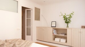 Un dormitorio con cama, armario, espejo, planta y un cuadro en la pared.
