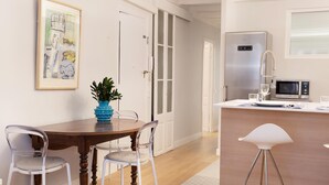 Una cocina moderna con una mesa de comedor de madera, sillas blancas y un jarrón azul.