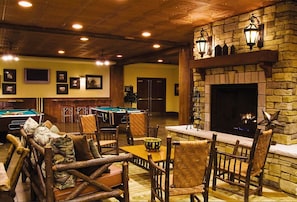 Relax in the lounge area with a pool table, comfortable seating, and a stone fireplace.