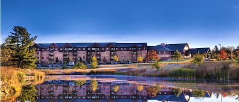 A hotel with multiple buildings, a large reflective pond, and surrounding trees.