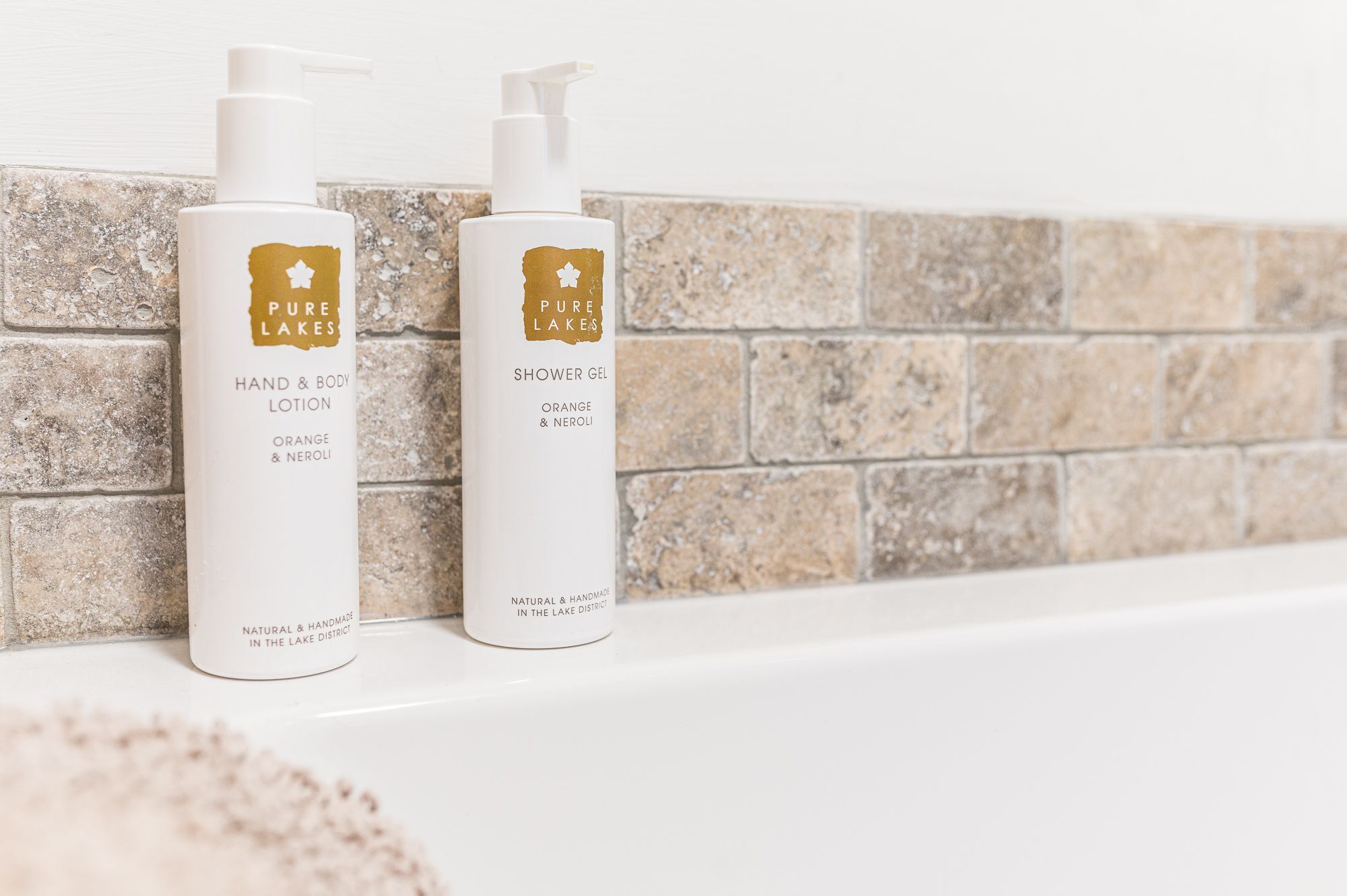Two bottles of hand and body lotion and a shower gel on a white shelf against a textured wall.
