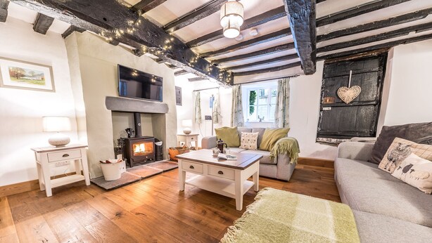 A cozy living room with a fireplace, wooden floors, a sofa, a table, and a TV. - Beautiful, 17th century Lake District cottage close to village and mountains (Coniston)
