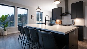 Una cocina moderna con una isla grande, taburetes de bar y vistas a árboles a través de amplias ventanas.