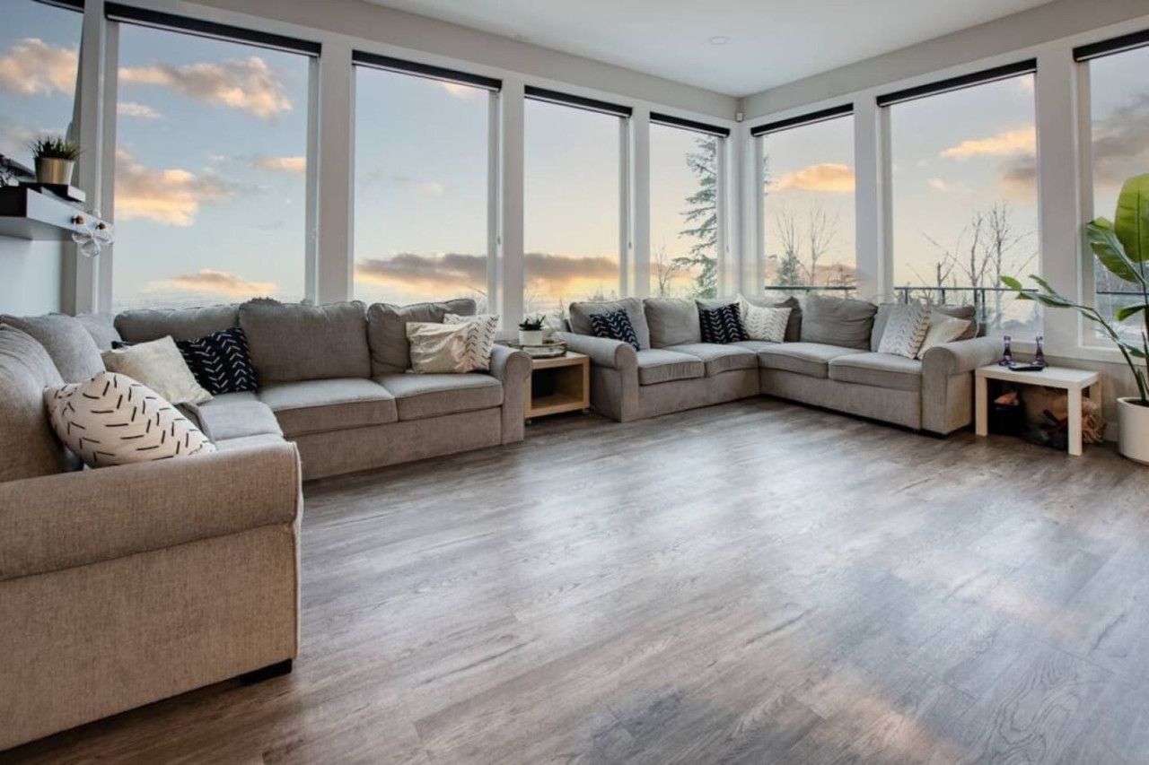 A modern living room with a sectional sofa, large windows, and a view of the sky.