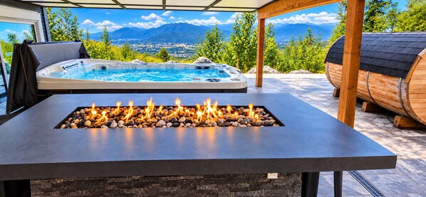 A hot tub with a mountain view, a fire feature with stones, and a wooden barrel.