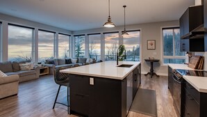 Una cocina moderna con una isla grande, un área de comedor con sofá y ventanas amplias que ofrecen vistas al exterior.