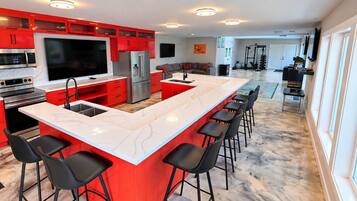 A modern kitchen with red cabinetry, a large island with bar stools, and a built-in TV.