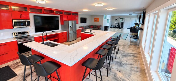 A modern kitchen with red cabinetry, a large island with bar stools, and a built-in TV.