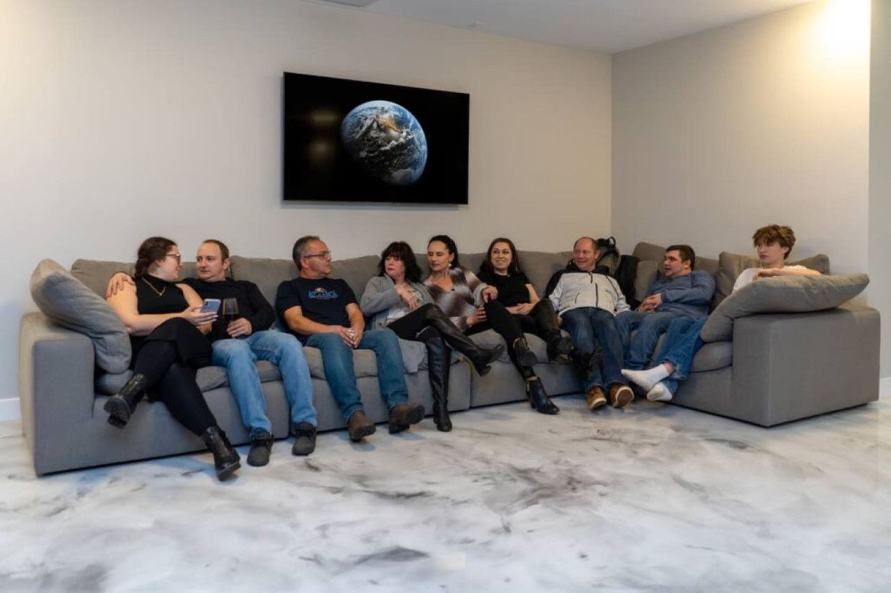 A group of people seated on a grey sofa in a room with a marble floor and a large picture of Earth on the wall.
