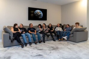 A group of people seated on a grey sofa in a room with a marble floor and a large picture of Earth on the wall.