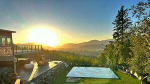 Un espacio moderno al aire libre con terraza de madera, un mapa grande y vistas a la ciudad y montañas al fondo.