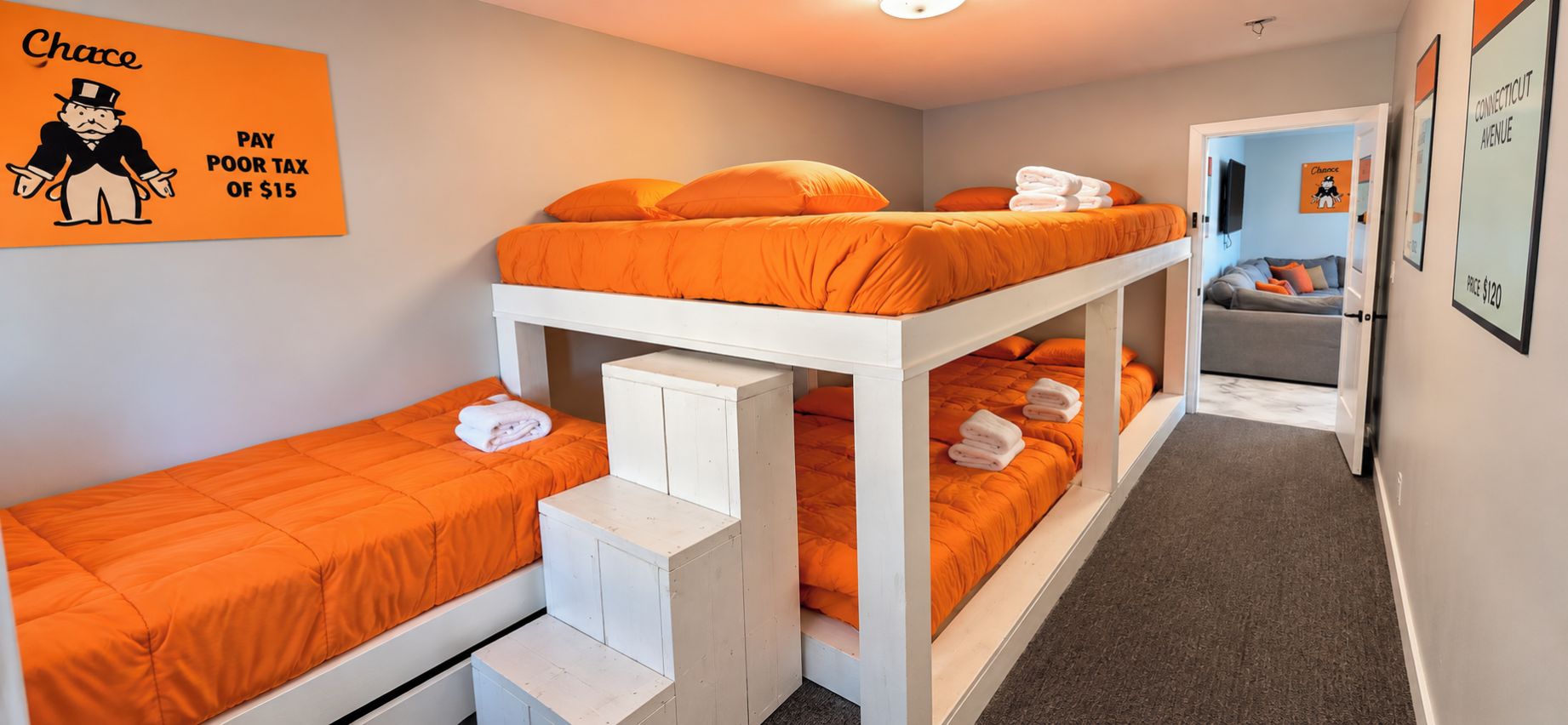 A dormitory room with bunk beds, a desk, and a chair. There is a poster on the wall and a door leading to another room.