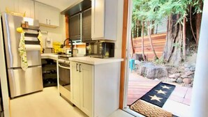 Una cocina moderna con electrodomésticos de acero inoxidable, armarios blancos y vistas a un área exterior ajardinada con un felpudo con diseño de estrellas en la entrada.
