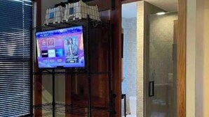 Un dormitorio con una cama, un televisor montado sobre un soporte de madera, una puerta corredera de vidrio que da al baño y un ventilador de techo.