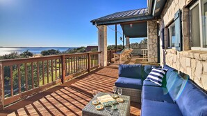 A wooden deck with a blue sofa and a table set for two, overlooking a scenic view. - Private Deck & Grill: Sunny Lakefront Escape (Burnet)