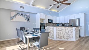 A modern kitchen with white cabinets, a central island, and a dining area with a table set for six. - Private Deck & Grill: Sunny Lakefront Escape (Burnet)