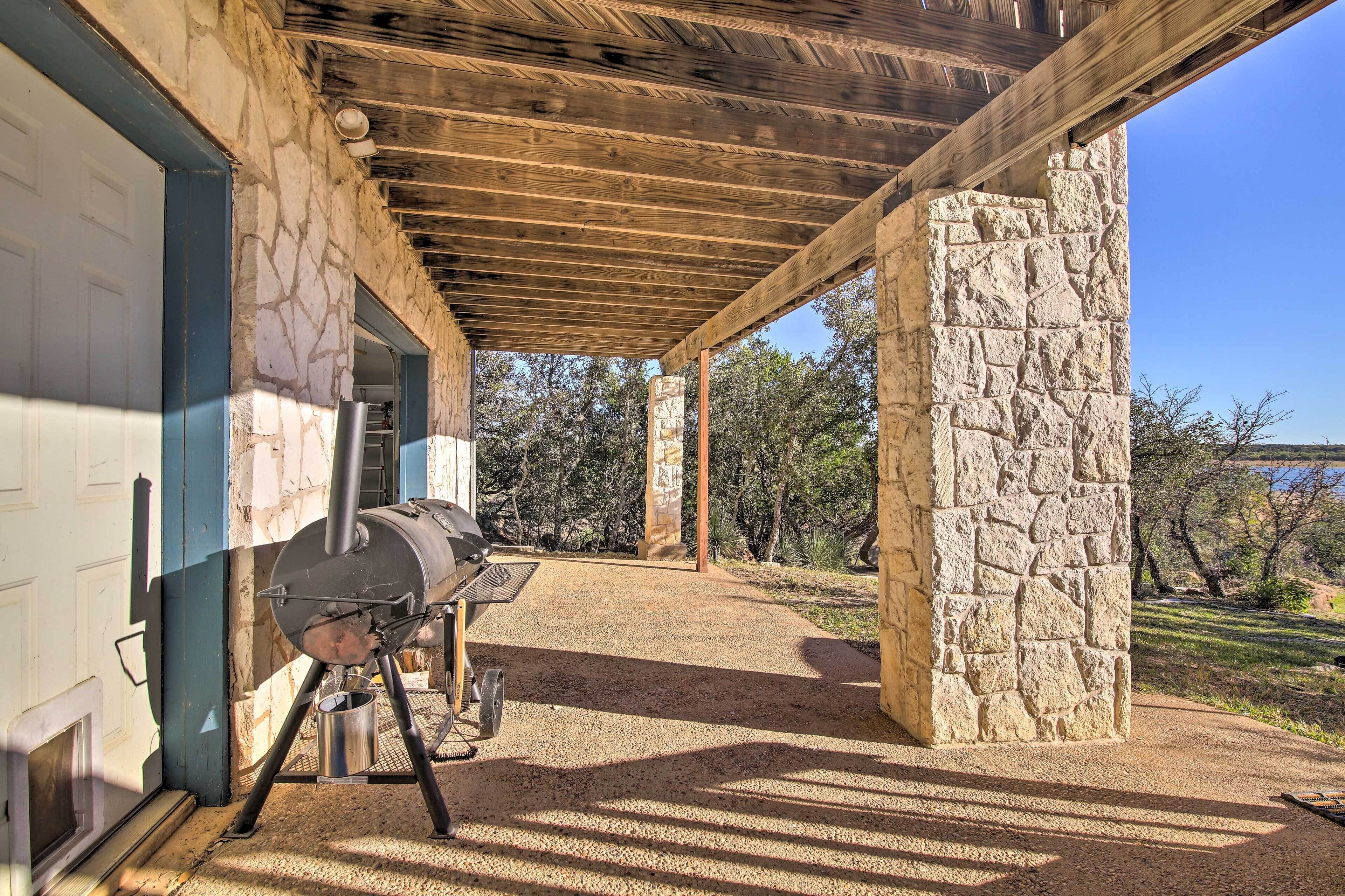 A covered outdoor area with a stone wall, a barbecue grill, and a gravel path leading to a door.