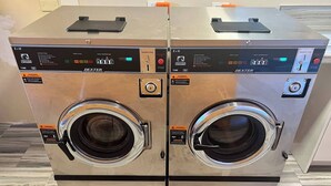 Two commercial front-loading washing machines with control panels, warning labels, and a warning label on the floor. - Relaxing 1Bed 1Bath Villa In Downtown Red Hook! (Saint Thomas)