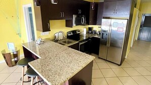 A kitchen with dark cabinets, a granite countertop, stainless steel appliances, and a trash bin. - Relaxing 1Bed 1Bath Villa In Downtown Red Hook! (Saint Thomas)