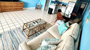 A living room with a sofa, coffee table, and a television. There is a kitchen area with cabinets and appliances. - Spacious 1Bed 1Bath Condo In Downtown Red Hook (East End)