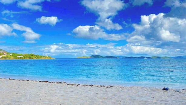 Una playa con agua azul cristalina y cielo parcialmente nublado.