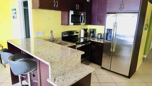 Cocina con alacenas de madera oscura, encimera de granito, electrodomésticos de acero inoxidable y una zona con taburetes de bar.