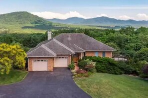 A single-story house with a garage, surrounded by lush greenery and hills in the background. - Amazing Mountain Views, Hot Tub and Close to Wineries and Breweries (Afton)