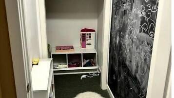 Un pasillo estrecho con un manto blanco de piel, una pequeña casa de juguete rosa y una pizarra con la palabra 'WELCOME' escrita.