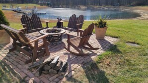A patio with Adirondack chairs, a fire pit, and a view of a lake. - Building Memories & Relationships enjoy stocked pond, woods, game room, and more (Holland)