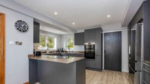 A modern kitchen with a central island, built-in oven, and stainless steel appliances. - Seahaven - Luxury Cottages (Torquay)