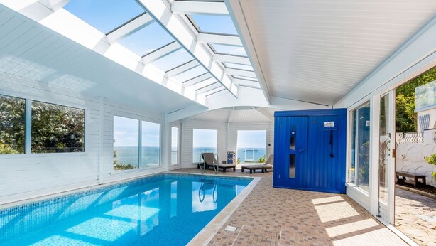 A swimming pool with a clear view of the sea, a blue door, and a tiled floor. - Seahaven - Luxury Cottages (Torquay)