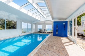 A swimming pool with a clear view of the sea, a blue door, and a tiled floor.