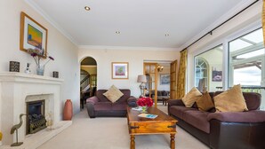 A spacious living room with two sofas, a wooden coffee table, a fireplace, and a large window offering a view. - Seahaven - Luxury Cottages (Torquay)