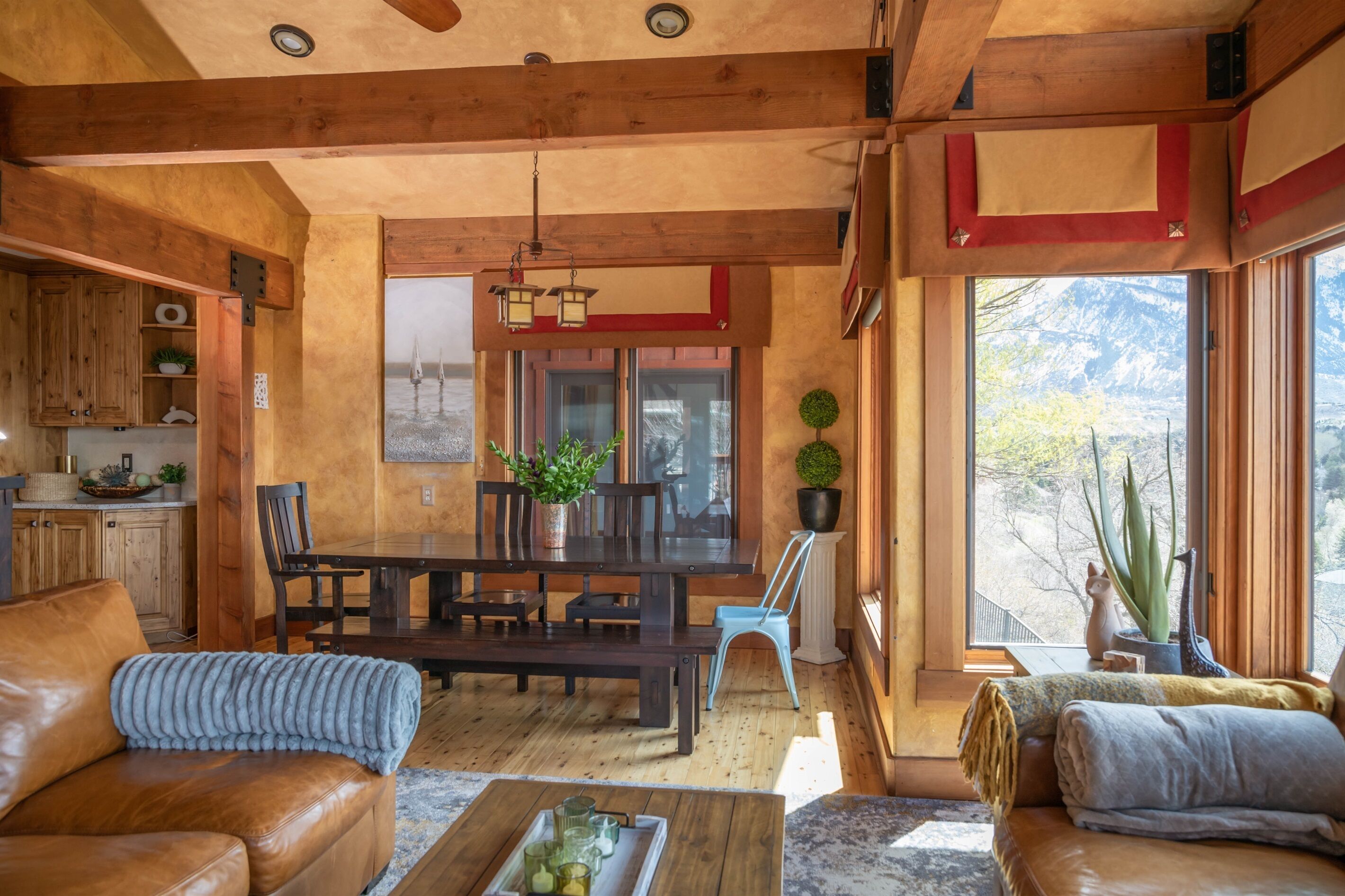 Una sala de estar acogedora con techo de madera, un comedor con mesa y sillas, y un ventanal con vistas a la montaña.